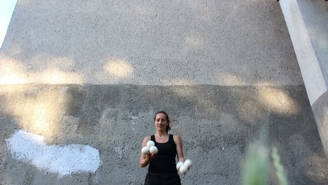 A professional circus actress juggles with white balls on the street.A professional juggler juggles with white balls. An attractive female juggler trains her juggling skills.