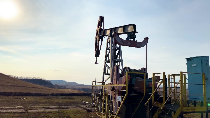 Machine for pumping oil and gas. Silhouette of a working oil pump from an oil field in the sun in a field. Industrial equipment. Side view.