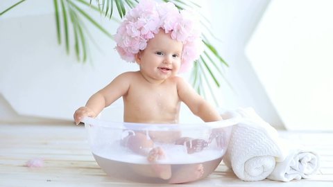 a child bathes in a basin with foam, a girl of 8 months plays in a bathing cap with water