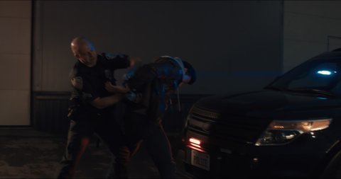 WIDE Police officer searches and handcuffs a suspect, African-American Black criminal. Police car lights flashing in the background. Shot with RED cinema camera and 2x Anamorphic lens