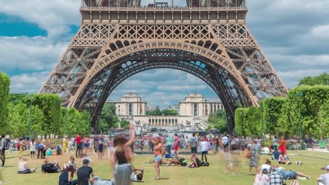 Champ de Mars and the Eiffel Tower timelapse in a sunny summer day. Paris, France. Green trees and cloudy sky, people sitting and walking around