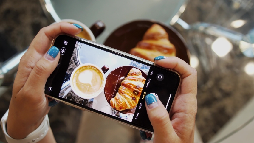 Close up of woman holds modern smartphone and taking pictures of her morning breakfast coffee and tasty croissant buns to share photos on social media resources | Shutterstock HD Video #1061947165