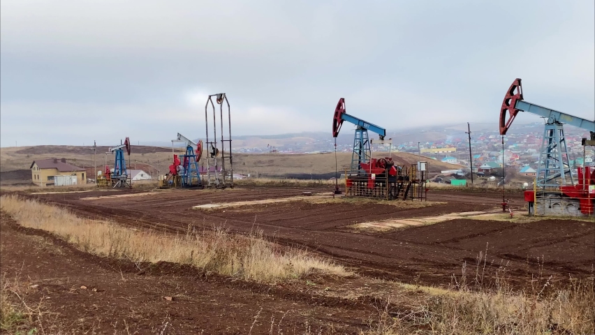 Three machines for pumping oil and gas. Silhouette of working oil pumps from a field in a foggy field against the background of grass and an industrial city. Equipment for oil and gas fields.