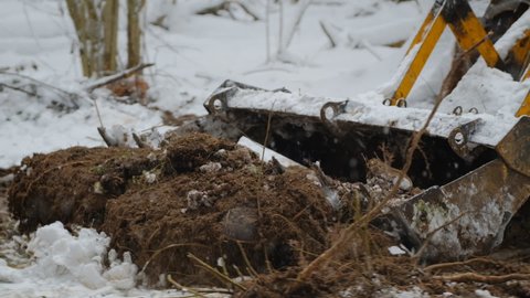 Bulldozer removes a layer of soil in a snowy forest. Bucket close up