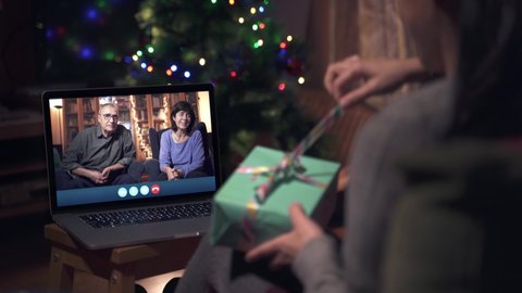 Family celebrating Christmas through a Video call. Parents online celebrating with family during X-mas holidays. Opening presents. Coronavirus celebrations maintaining the distance.
