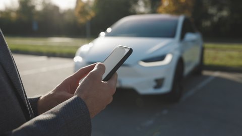 Person controls a self-driving electric car using mobile application. Autonomous autopilot driverless car. Smartphone app. Sensor scanning road ahead for vehicles, danger, speed limits