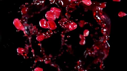 Ripe pomegranate grains are flying up with splashes of sweet juice on the black background in slow motion