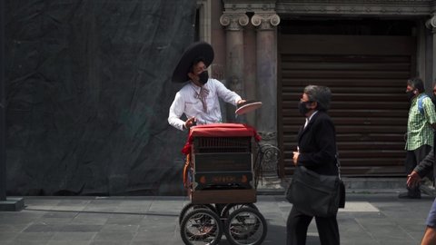 Mexico City, Mexico - September 3, 2020: 4k video of a Mexican organ grinder with a classic Mexican attire and a black face mask, playing a street organ