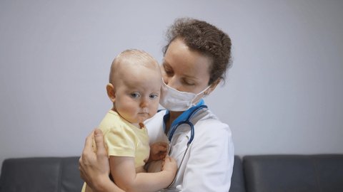 Nurse in face cover cuddling sad baby in arms to calm down and ease stress. Frontline healthcare workers help families during coronavirus threat
