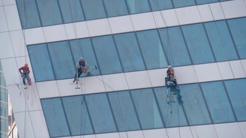 MOSCOW, RUSSIA - MAY 5, 2020: Team of professional washers cleaning modern office building skyscraper glass windows. Industrial climbing, occupation, architecture, dangerous job concept