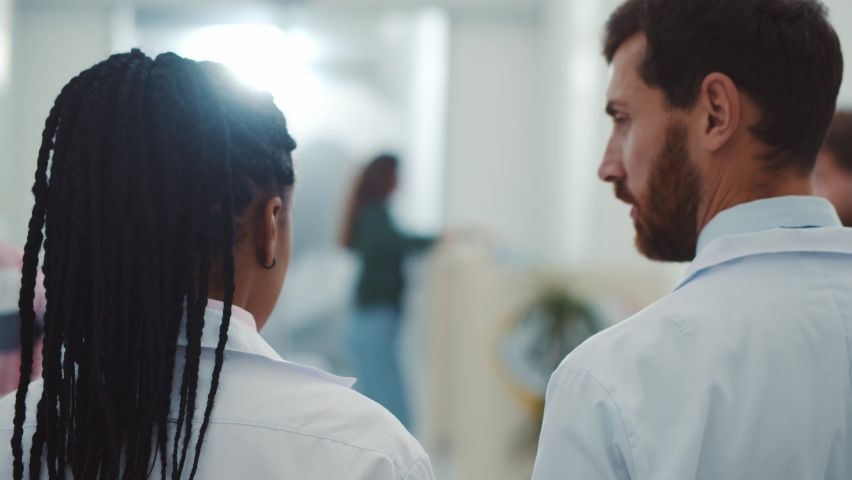 Close-up of chief doctor and female assistant afro-american woman walking along the corridor discussing patient medical report treatment indoors. Hospital environment. Healthcare workers. | Shutterstock HD Video #1061963920