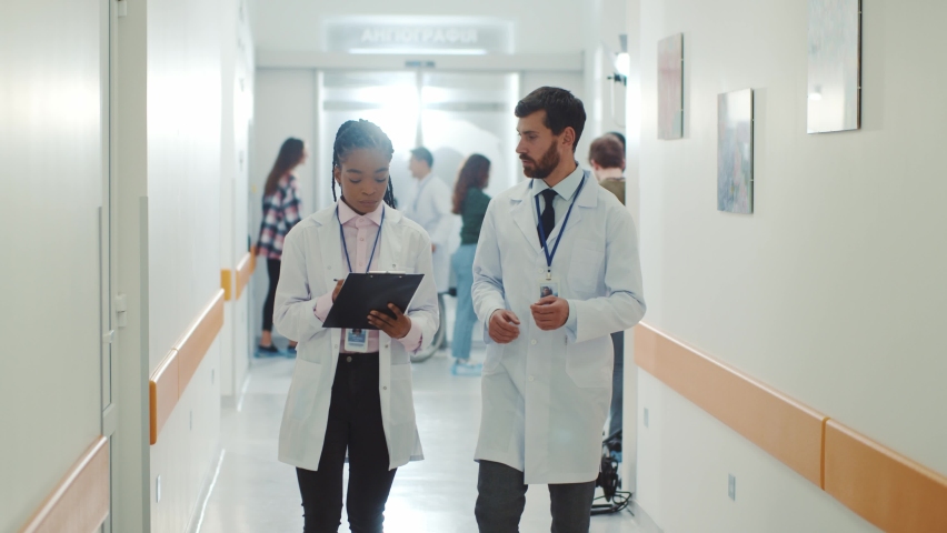Multi-ethnic couple african american doctor with caucasian bearded therapist walking along the corridor and talking. Coworkers. cooperation. Medical staff. Hospital. Royalty-Free Stock Footage #1061963929