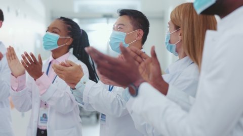Group of mixed-race professional doctors and assistants in masks clapping their hands celebrating salary increase business success at workspace meeting conference.