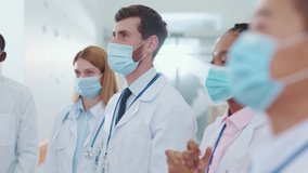 Multi-race professional medical doctors and assistants wearing protective masks against coronavirus applauding on team conference business employment meeting in corridor. Cooperation and success. - Powered by Shutterstock - Get 15% off with code: PIKWIZARD15