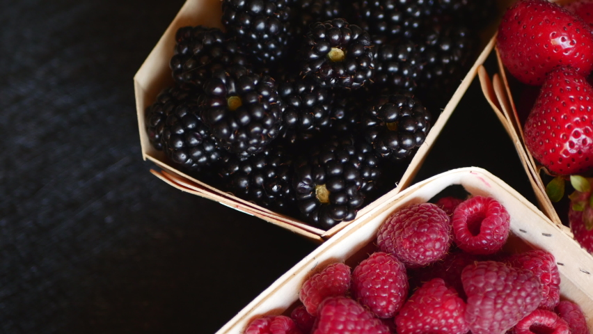 Close Up Of Overhead View Of Fresh Strawberries, Blackberries And Raspberries In Tray For Sale Lying On A Black Background Of Store Counter. Slider Shot.