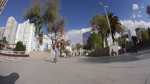 La Paz / Bolivia - August 13 2016:  Young Long Hair Hispanic Skateboarder in Brown T-Shirt is Jumping over a Wheel