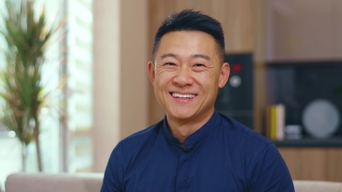 Smiling asian chinese man look at camera happy at home. Feel confident. Young japanese korean discussion casual relax face communication. Slow motion