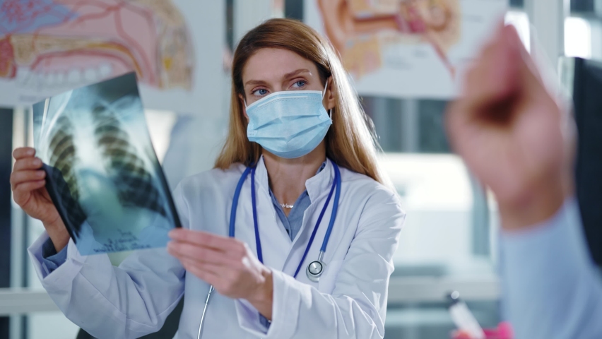 Face woman doctor with medical mask explain x-ray chest result speaking with illness man patient in examination room in hospital. Pandemic coronavirus therapy. Slow motion | Shutterstock HD Video #1061966344