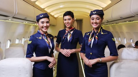 Team of diverse flight attendant posing with smile at middle of the aisle inside aircraft with passengers seated on the background