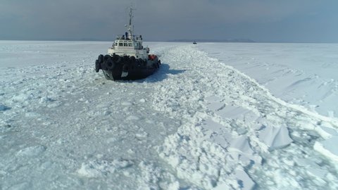 Aerial front of two icebreaker equipped ships sails off coast of an abstracted costal city, breaks frozen ice. Snow-capped endless sea winter cold. Shipping, navigation. Sunny day horizon. Open space
