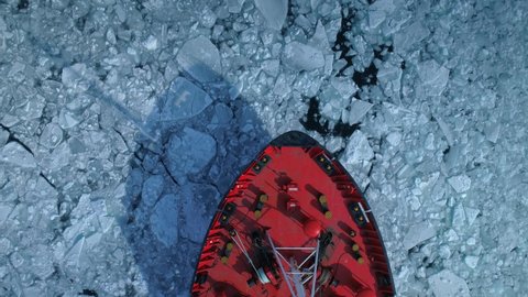 Drone top down Epic red steel icebreaker ship tanker breaks winter frozen sea, overcomes. Bow of ship floats through ice floe. Huge white block of ice. Sailing, navigation. Unique Polar expedition. 4k