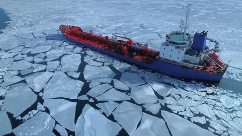 Aerial above epic huge steel icebreaker breaks ice by bow of ship and floats in large sea ice floes. Maintaining navigation in a frozen sea channel laying. Self-propelled specialized vessel red ship