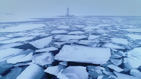 Drone approach to old Vladivostok Tokarevsky lighthouse. Unique heavy snowfall, blizzard dramatic winter storm. Snowy dark frozen sea. Huge beautiful blue ice. People stand on edge of spit. Travel 