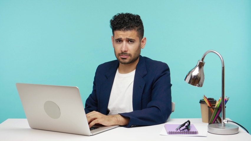 Crazy angry man pointing finger at his nose and at you, blaming in lie and dishonest, sitting at desk in his office. Indoor studio shot isolated on blue background | Shutterstock HD Video #1061978590