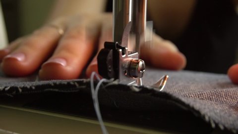 The seamstress sews denim on a sewing machine, advances the fabric with his fingers. Close-up. The movement of the foot and needle when sewing denim on the sewing machine.