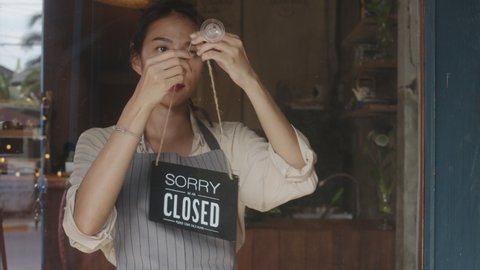 Young Asia manager girl turning a sign from open to closed sign on glass door cafe after coronavirus lockdown quarantine. Owner small business, food and drink, business financial crisis concept.