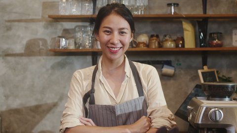 Portrait young Asian woman barista feeling happy smiling at urban cafe. Small business owner Indonesian girl in apron relax toothy smile looking to camera standing at the counter in coffee shop.