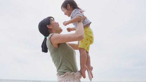 Asian family on vacation. Beautiful mother giving warm hugs little baby girl in arms and kiss then raise kid in the air on the beach. Soft touch, love care, protection of mom and child relationship.