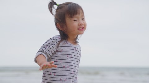 Portrait of Asian little cute baby girl dancing on the beach. Young small kid feeling happy and smile on family trip vacation at the sea. The adorable child looking at camera with smile face. 