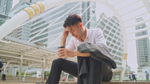 Asian business man feeling sad after unemployment from his company. The man sitting outdoor    feeling stress worry about losing the job due to world economic problem from covid crisis concept.