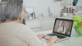 Asian senior woman video call with doctor in living room at home. Elder patient consulting with general practitioner application computer laptop. Doctor and Consultant online and telemedicine concept.