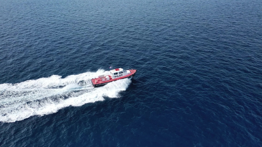 Aerial drone tracking video of red pilot boat cruising in high speed in Mediterranean deep blue sea offering navigational aid to ships | Shutterstock HD Video #1061995225