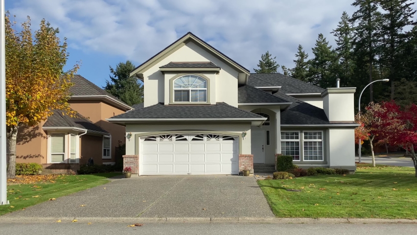 Establishing shot of two story stucco luxury house with garage door, red and yellow trees and nice landscape in Vancouver, Canada, North America. Day time on September 2020. Still camera view. H.264.
