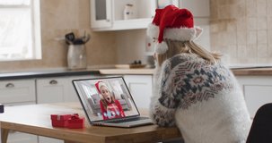 Rear view of caucasian woman in santa hat having a video chat with another woman in santa hat opening gift box on laptop at home. social distancing quarantine lockdown during coronavirus pandemic