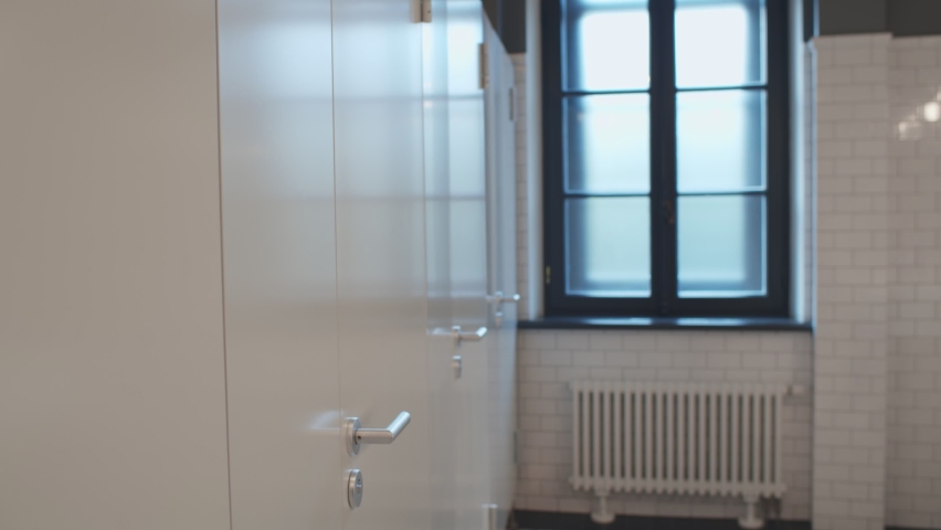 Students in mask visiting restroom in college and washing hands with soap. Side view of asian college guy with backpack in safety mask leaving bathroom stall and washing hands