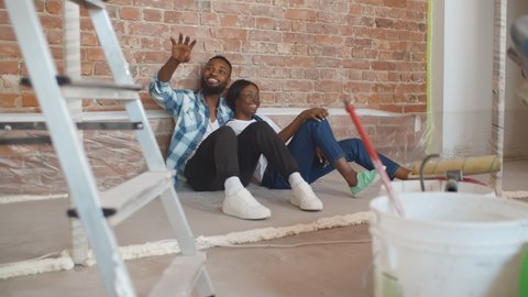 African couple sitting on floor in empty room of new home planning design. Portrait of cute afro-american couple relaxing on floor in redecorating apartment
