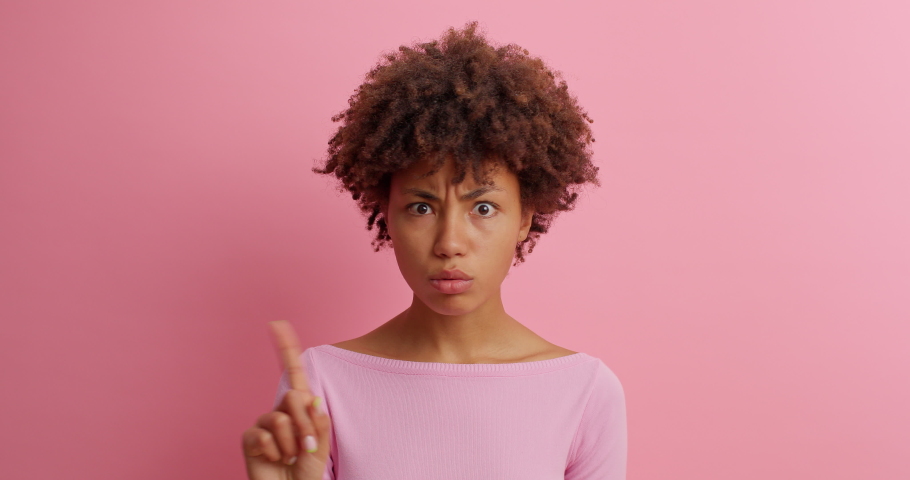 Serious young woman shakes finger and says no I dont need drressed in casual clothing poses against pink background doesnt like plan scods for bad choice prohibits action isolated on pink wall | Shutterstock HD Video #1062004837