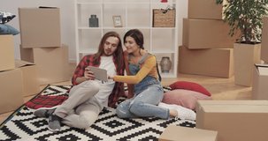 Beautiful caucasian young couple taking selfie and shooting video on tablet sitting on carpet in new apartment.