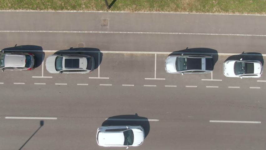 AERIAL, TOP DOWN: Flying above an autonomous car successfully parallel parking into a vacant spot at the side of a road. High-tech self-steering vehicle parks itself into empty roadside parking spot. Royalty-Free Stock Footage #1062009271