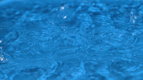 SLOW MOTION, MACRO, DOF: Detailed shot of drops of rain falling into a vibrant light blue pool. Countless raindrops fall into an empty pool in someone's backyard. Close up view of torrential rain.