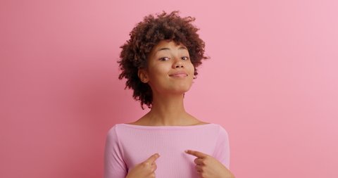 This is me. Self confident serious woman in casual clothing points at herself being proud of own achievements poses against pink background. Assertive boastful lady brags her accomplishments