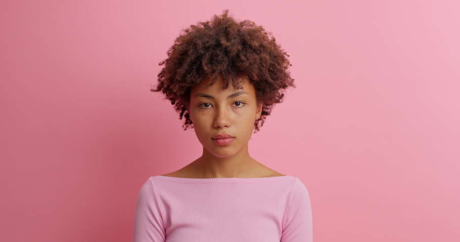 Bewildered confused dark skinned woman has doubts and hesitation about something looks at different sides cant make right decision poses against pink background. Confused Afro American girl. Royalty-Free Stock Footage #1062011065