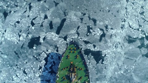 Flight top down epic green huge cargo reefer ship bulk carrier floats frozen sea, breaking through ice. Unique winter cracked ice pattern. Expedition to North. Logistics delivery transportation. Drone