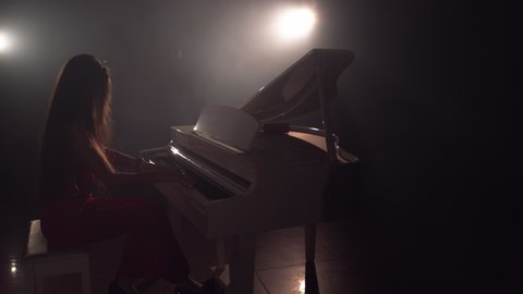4K Footage Of Female Pianist Plays In Beautiful Grand Piano On Stage In Concert . A woman plays the piano in the concert hall. Stage light and light fog on the background
