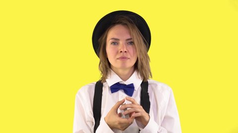 Woman Croupier shuffles a deck of cards in her hands. Dressed in a Hat, bow tie, suspenders. Yellow background, 4k quality, gambling concept.