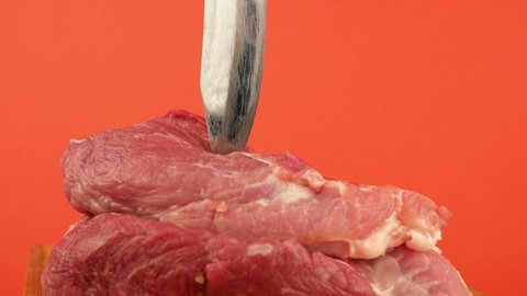 A sharp large butcher's knife is stabbed into raw red meat. Pieces of fresh pork and a knife on a bright orange background. The theme of cooking meat and meat products. Sausage shop. Selective focus